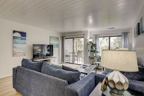 Una sala de estar moderna con un televisor de pantalla plana, sofás grises, una mesa de centro y un ventanal con cortinas.