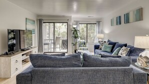 A living room with a sofa, TV, and a balcony with a view of palm trees.