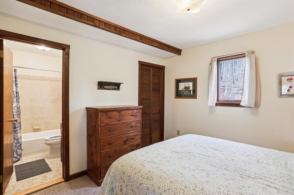 Un dormitorio con cama, cómoda de madera, un cuadro enmarcado y ventana con cortinas.