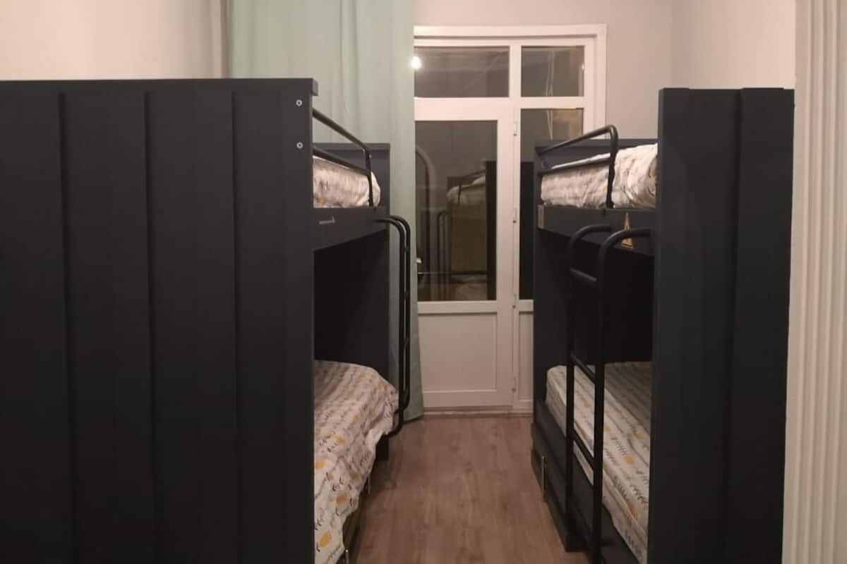 Ein schmales Zimmer mit Stockbetten, einer Tür und einem Fenster.