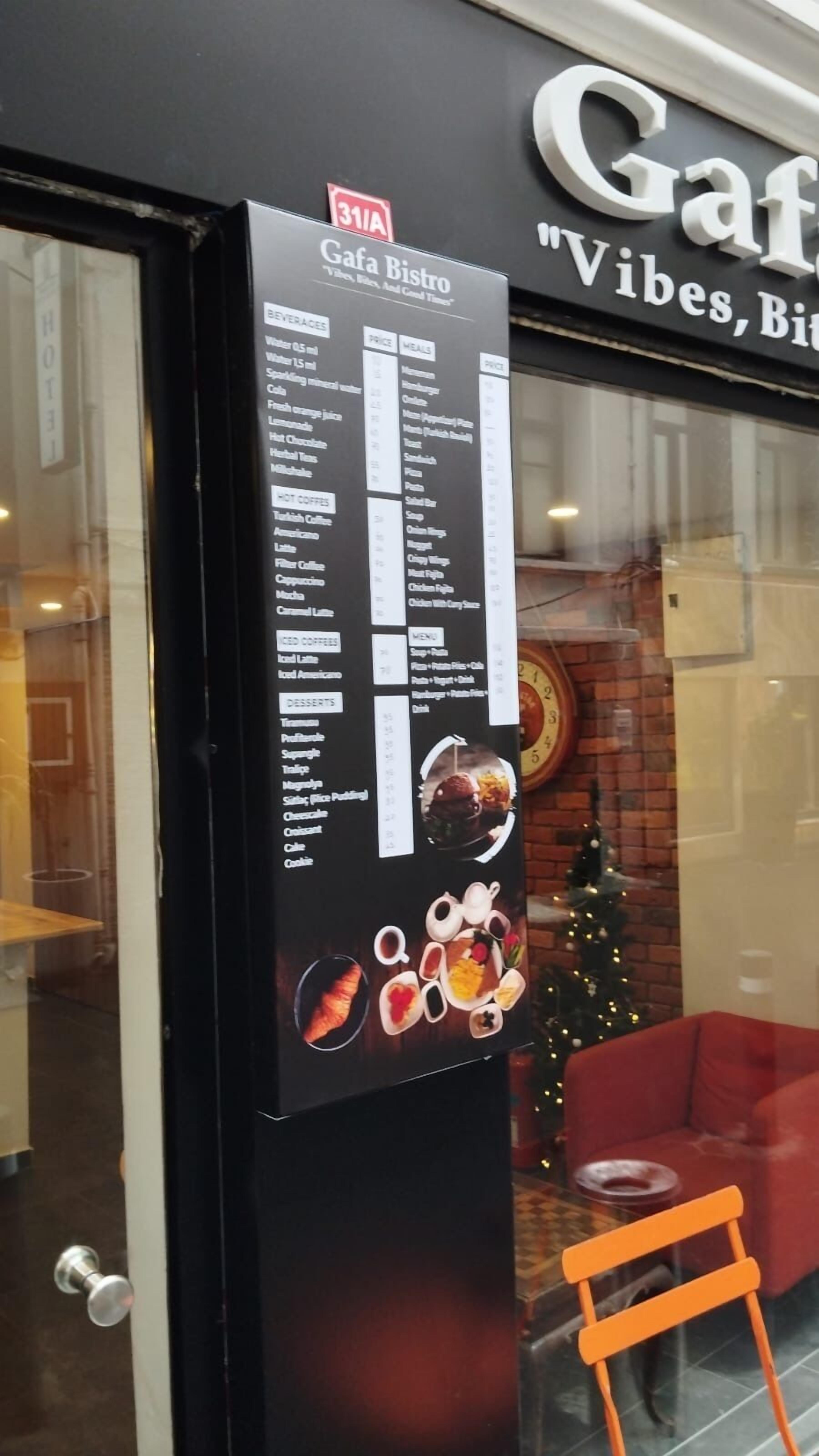 Un cartel de menú fuera de una cafetería, con un árbol de Navidad y una silla roja visibles en el interior.