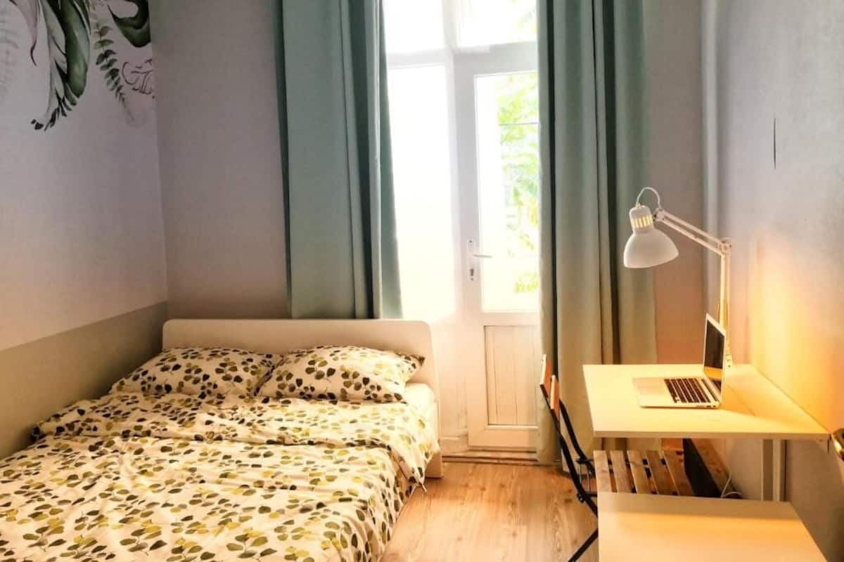 Ein Schlafzimmer mit einem Bett, einem Schreibtisch mit einem Laptop und einem Fenster mit Vorhängen.