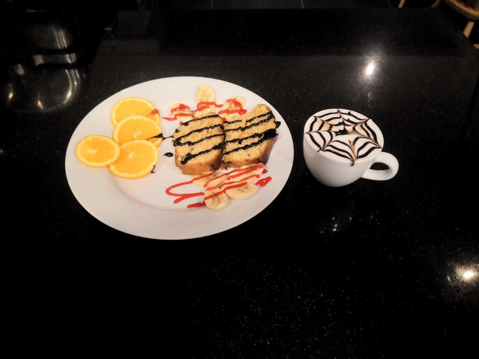 A plate with pastries, sliced bananas, and orange slices, and a cup of coffee with a chocolate design.
