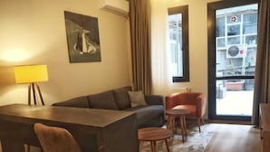 A modern living room with a sofa, a small table, and a chair. There is a painting on the wall and a window with curtains. - Gafa Garden Hostel & Apartments (Istanbul)