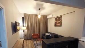 A compact living space with a wooden floor, a dining area with a black marble table, a sofa, and a single orange chair. - Gafa Garden Hostel & Apartments (Istanbul)