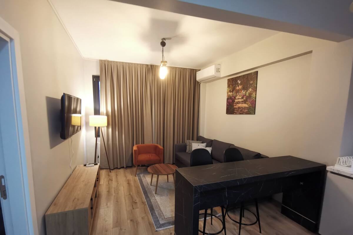 Ein gemütlicher Wohnraum mit Holzboden, einem Essbereich mit Tisch aus schwarzem Marmor, einer Couch und einem einzelnen orangefarbenen Sessel.