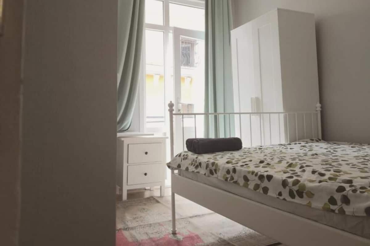 Ein Schlafzimmer mit einem Bett, einem Nachttisch, einem Kleiderschrank und einem Fenster mit Vorhängen.