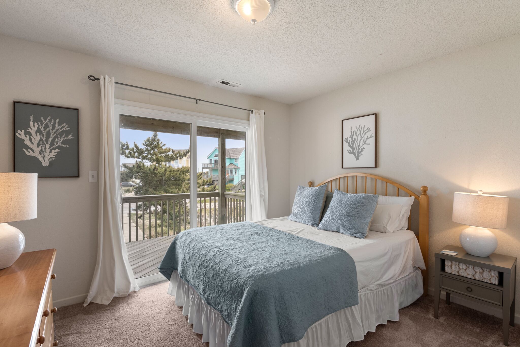 A bedroom with a bed, a nightstand, a window with curtains, and artwork on the walls.