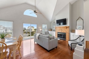 A spacious living room with a high ceiling, a fireplace, a television, and a balcony with large windows.