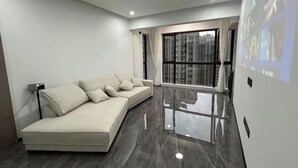 A modern living room with a sofa, a large window, and a projector screen displaying images.