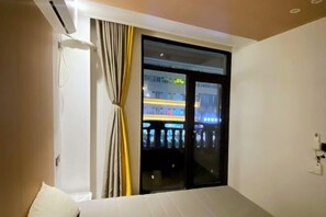 A hotel room with a bed, a window with curtains, and a view of a building with illuminated windows. - My House (Pingtan County)