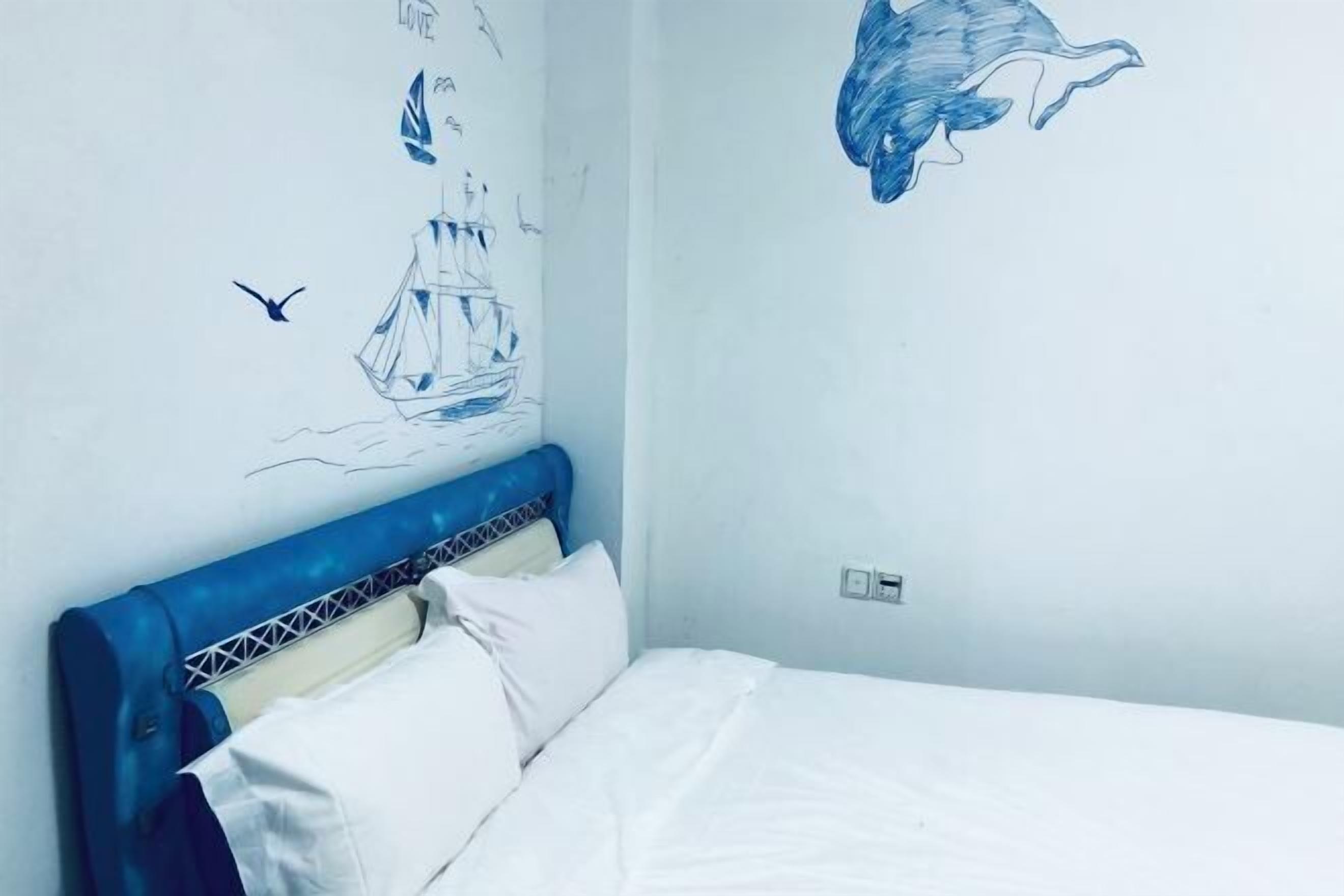 A bedroom with a bed, a blue headboard, and wall art including a ship and a dolphin.
