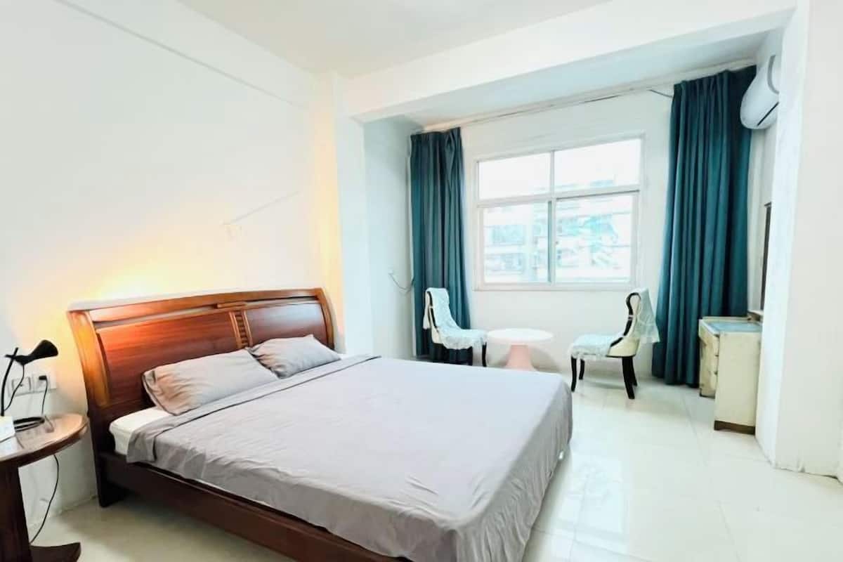 A hotel room with a wooden bed, a small round table, a chair, and a window with curtains.