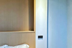 A hotel room with a wooden panel wall, a white door with a light switch, and a bed with a white sheet. - My House (Pingtan County)