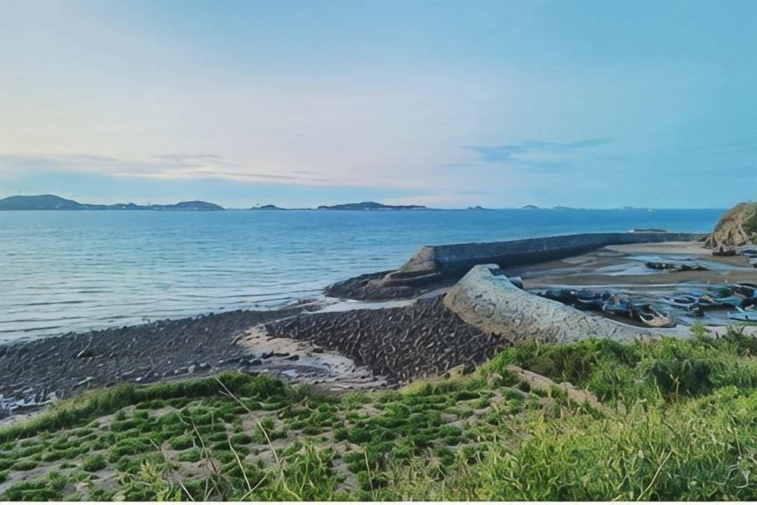A coastal landscape with a rocky shoreline, calm water, and distant landforms.