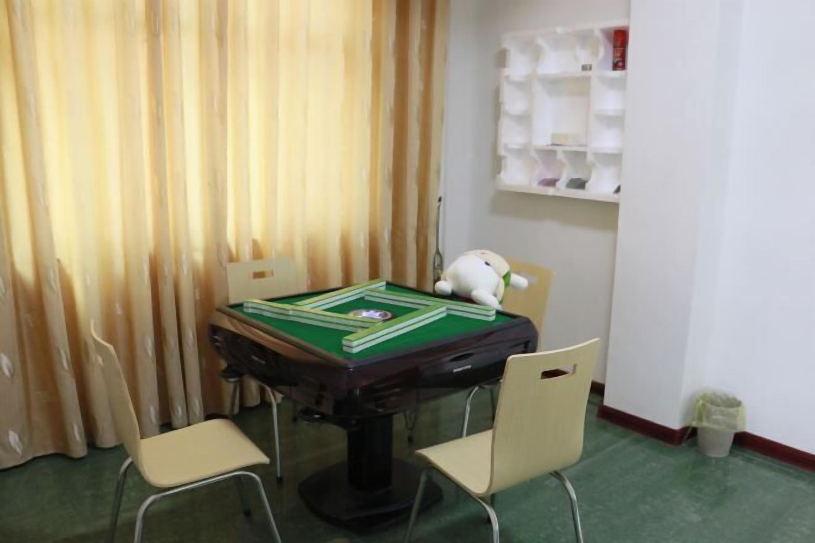 Una habitación con una mesa verde para juegos de mesa, dos sillas, un peluche blanco y un estante con objetos blancos.