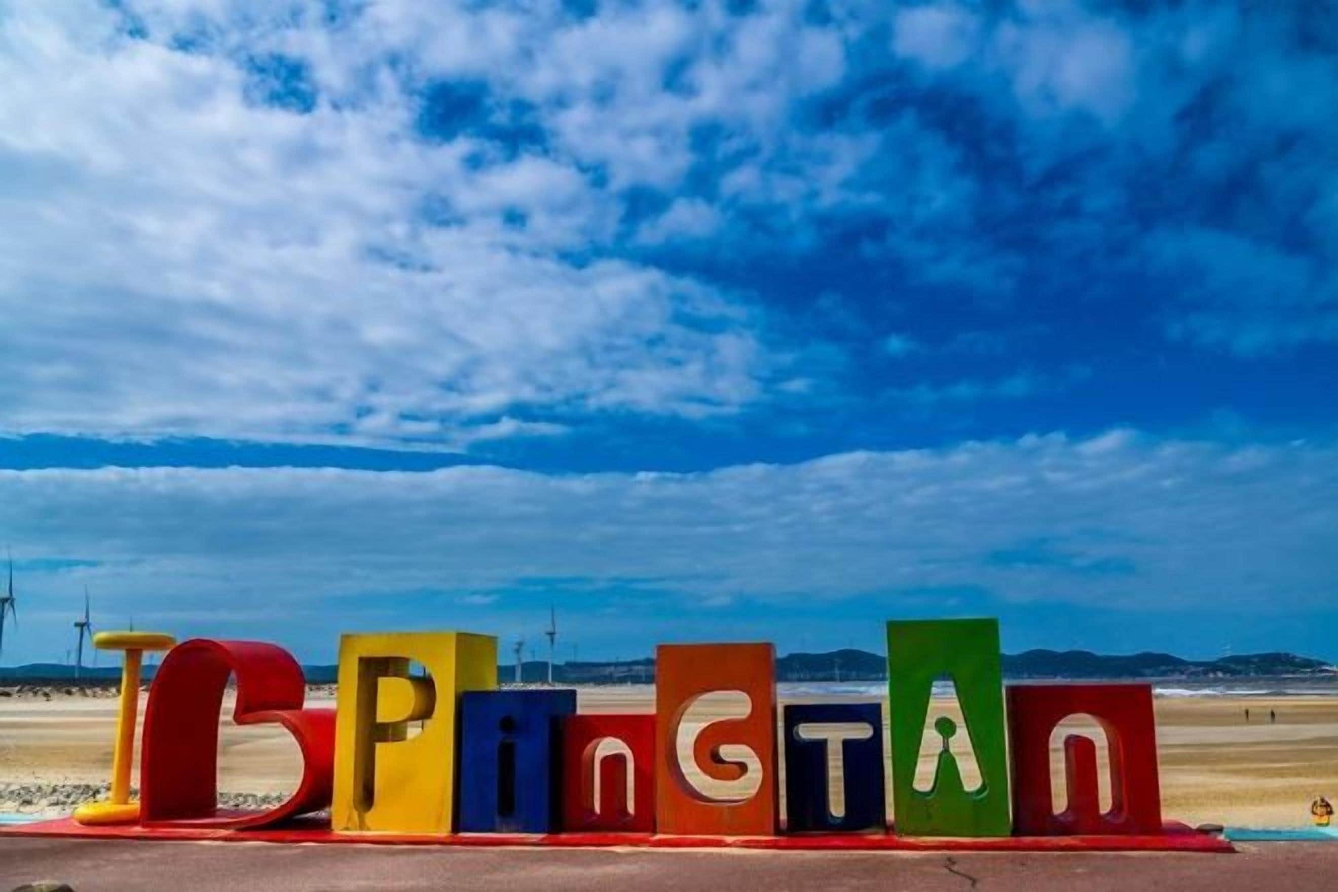 Colorful letters spelling 'TOPPING' on a beach with a clear sky.