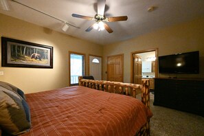 Une chambre à coucher avec un lit, un ventilateur de plafond, une télévision et un tableau encadré au mur.