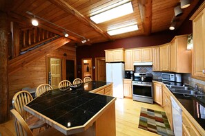 A kitchen with wooden cabinets, a black countertop, and a dining area with chairs. - Secluded Mountain Cabin 30 Min to Yellowstone (Island Park)