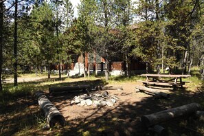 A rustic cabin with a wooden deck, surrounded by dense pine trees. - Secluded Mountain Cabin 30 Min to Yellowstone (Island Park)