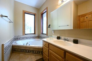 Une salle de bain avec une baignoire, un lavabo, des meubles en bois et une fenêtre.