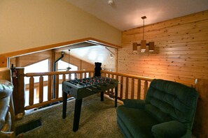 A cozy room with a foosball table, a green armchair, wooden walls, and a wooden railing.