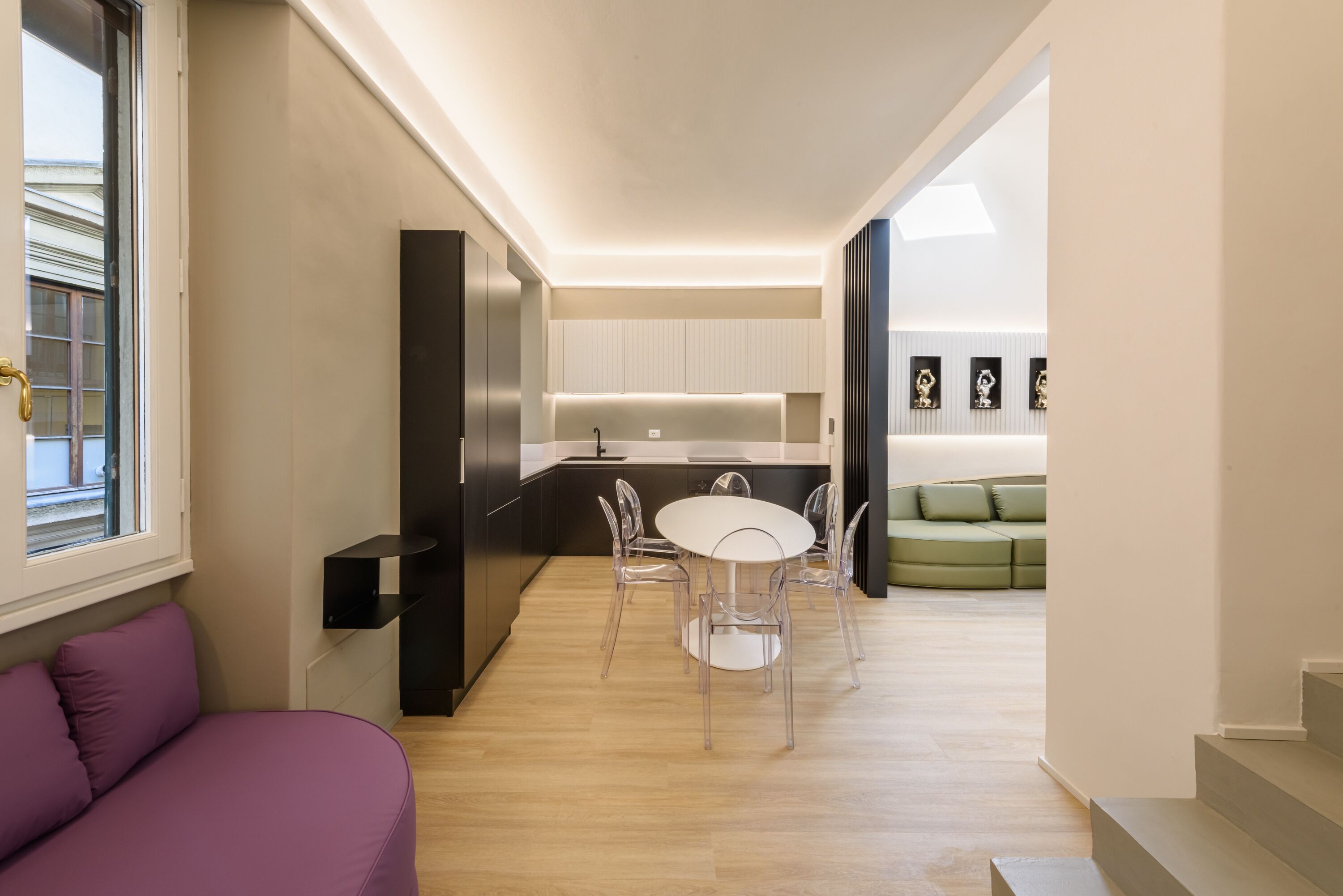A modern kitchen with a central island, a dining area with a round table and chairs, and a green sofa in a living area.