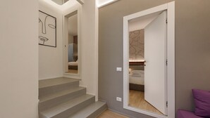 A modern interior with a staircase, a door leading to a bedroom, and a purple couch. - Anguillara Full Design by Mmega (Florence)