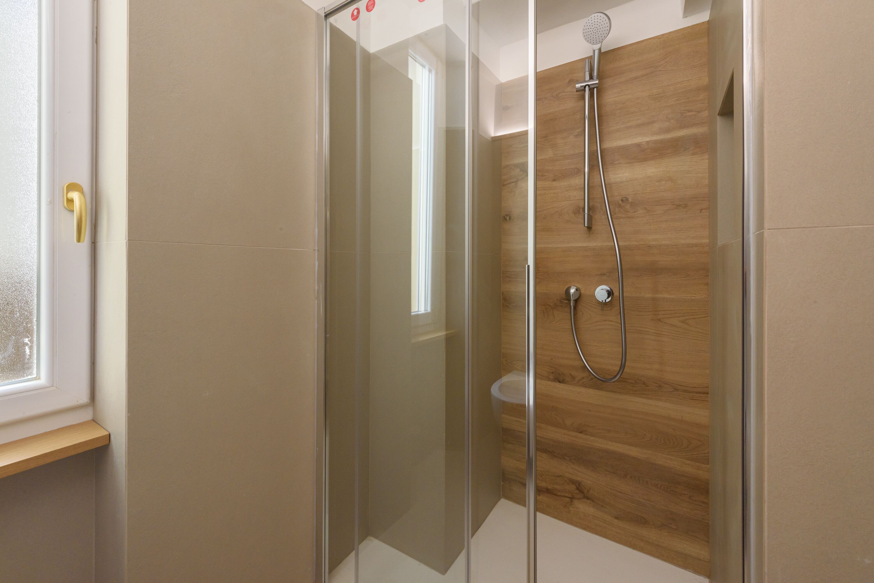 Een moderne badkamer met een douchecabine van glas, houten wandbekleding en een zichtbaar toilet.