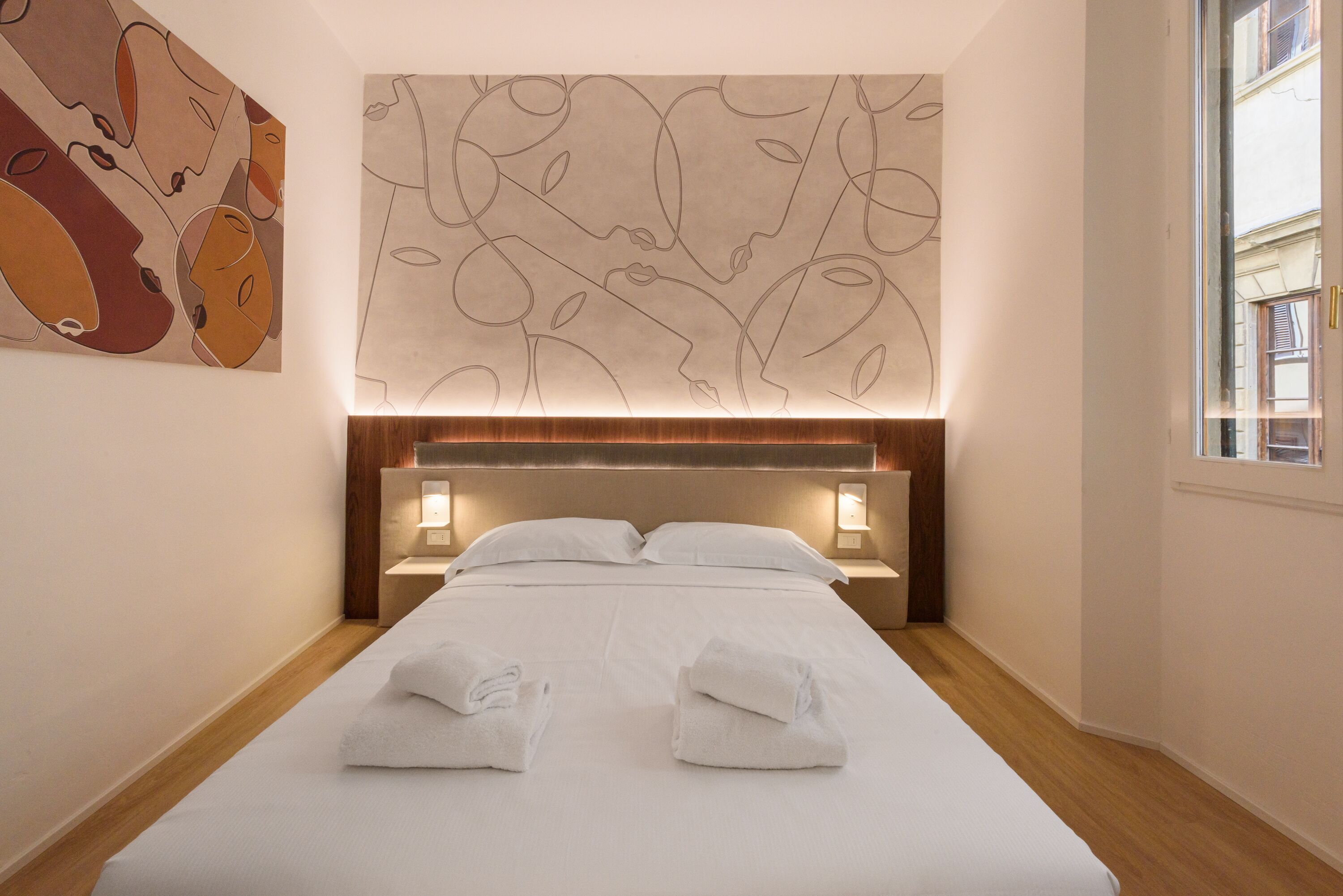 Habitación de hotel con una cama bien hecha, dos lámparas de noche y una gran obra de arte abstracta en la pared.