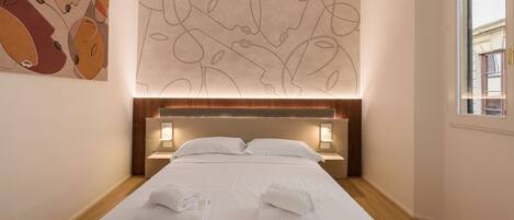 Habitación de hotel con una cama bien hecha, dos lámparas de noche y una gran obra de arte abstracta en la pared.