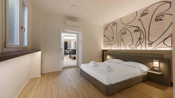 A modern bedroom with a large bed, bedside lamps, and a wall art piece. - Anguillara Full Design by Mmega (Florence)