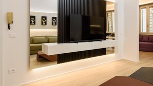 A modern living room with a flat-screen TV mounted on a white console, a green sofa, and a purple sofa. - Anguillara Full Design by Mmega (Florence)