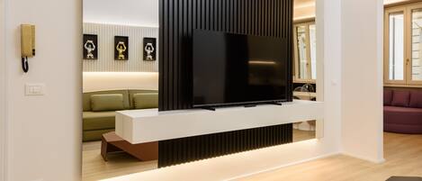 Una sala de estar moderna con un televisor de pantalla plana montado en una consola blanca, un sofá verde y un sofá púrpura.