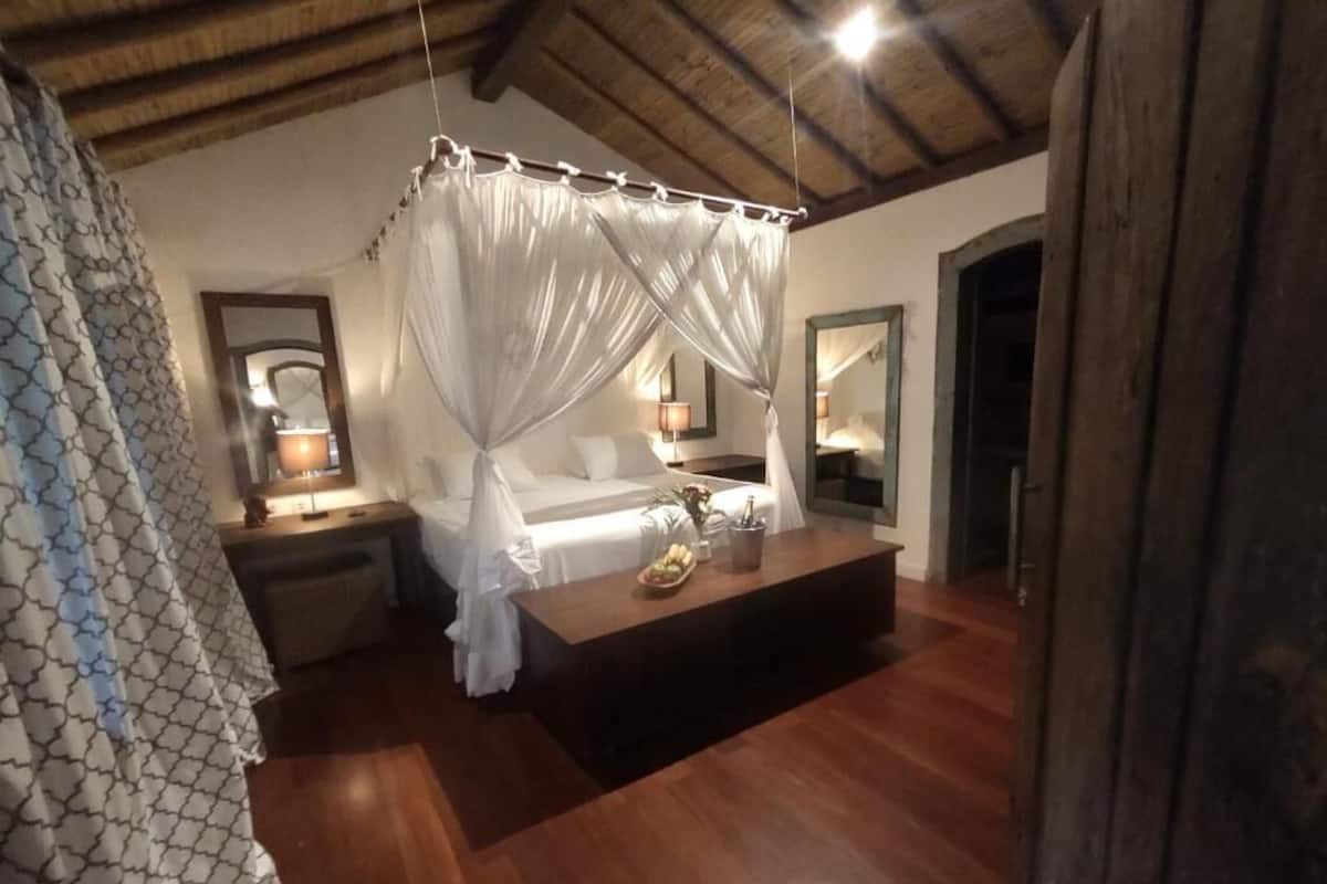 A bedroom with a canopy bed, wooden flooring, a bedside table with a lamp, and a nightstand.