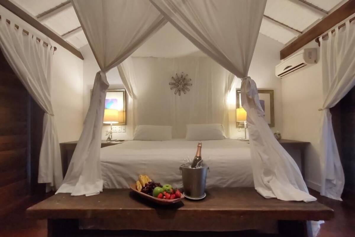 A bedroom with a canopy bed, a bedside table with fruit and a bottle of champagne, and two bedside lamps.