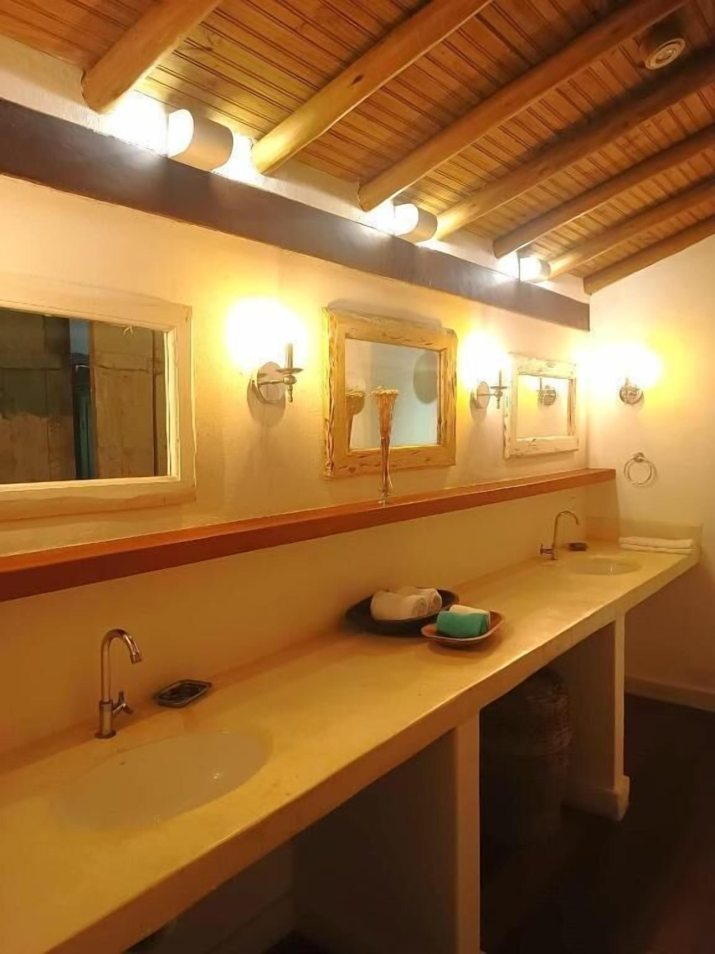 Casa de banho com duas pias, vigas de madeira no teto e luzes na parede.