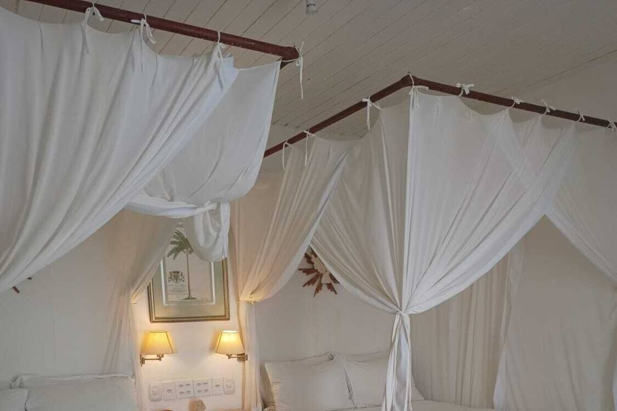 A room with two beds, each with a canopy. There are bedside tables with lamps and a framed picture on the wall.