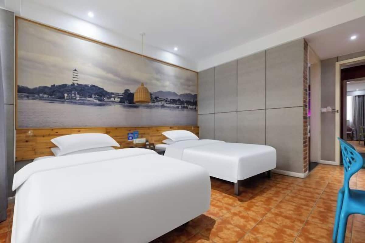 Habitación de hotel con dos camas, un mural grande en la pared y un baño visible a través de una puerta abierta.