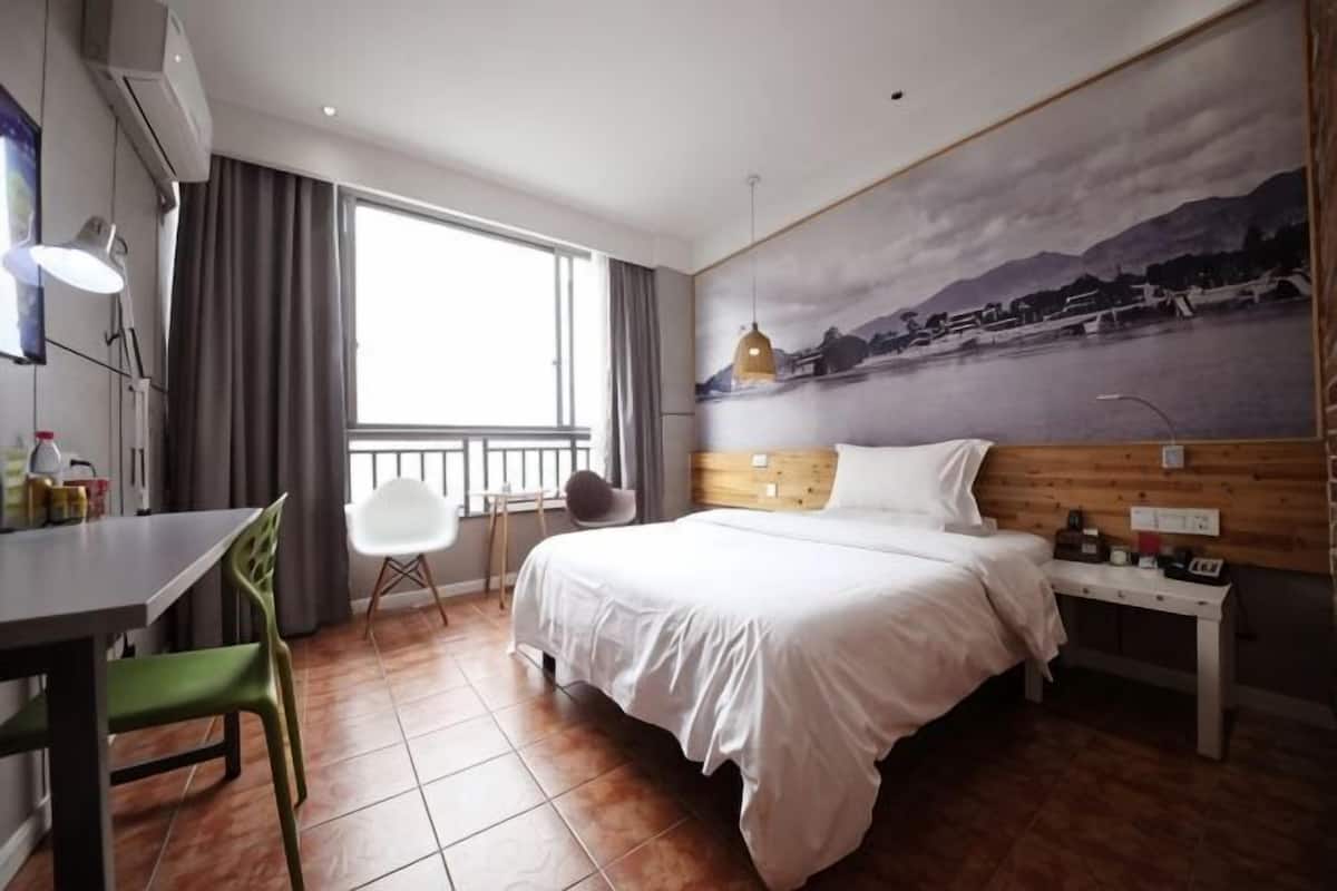 Habitación de hotel con cama, escritorio, silla, mesita y un cuadro en la pared.