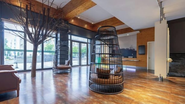 Un hallo espacioso con techo de madera, ventanas amplias y un área de estar central con una escultura de árbol y una estructura espiral de metal negro.