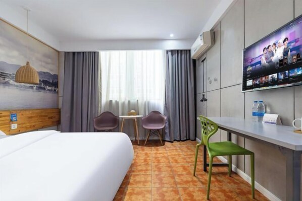 Quarto de hotel com cama, escrivaninha com cadeira, televisão e janela com cortinas.