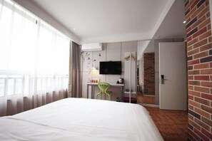 A hotel room with a bed, a desk with a chair, a television, and a brick wall. - Tuke Global Hotel (Wenzhou Louqiao South Railway Station) (Wenzhou)