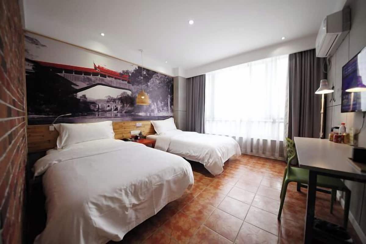 Una habitación de hotel con dos camas, una mesa de comedor, un televisor y un mural en la pared.