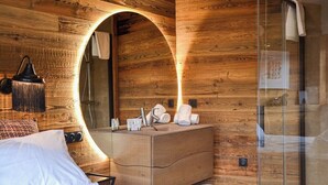 Ein modernes Badezimmer mit Holzwänden, einer Duschkabine aus Glas, einem Holzwaschtisch mit Spiegel und einem Bett mit weißen Leinen.