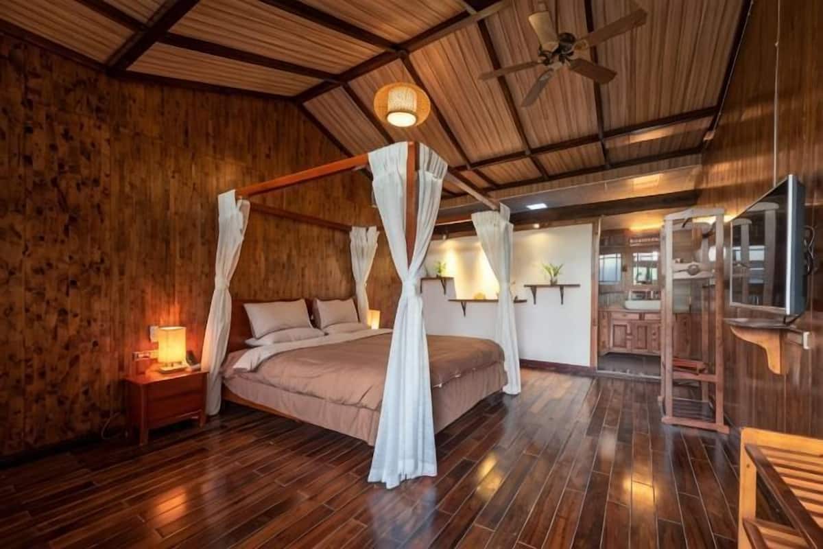 A wooden-paneled room with a four-poster bed, a ceiling fan, and a television.
