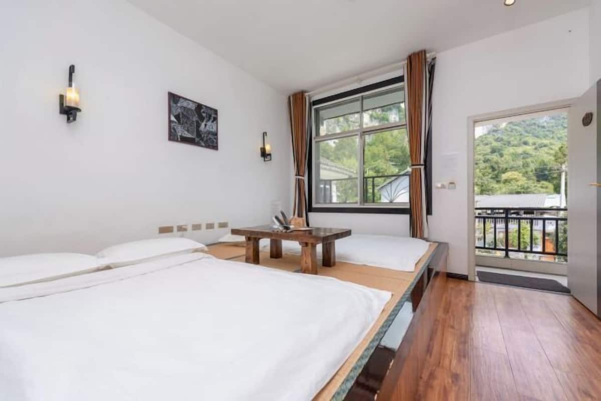 A hotel room with two beds, a small table, a window with curtains, and a balcony.