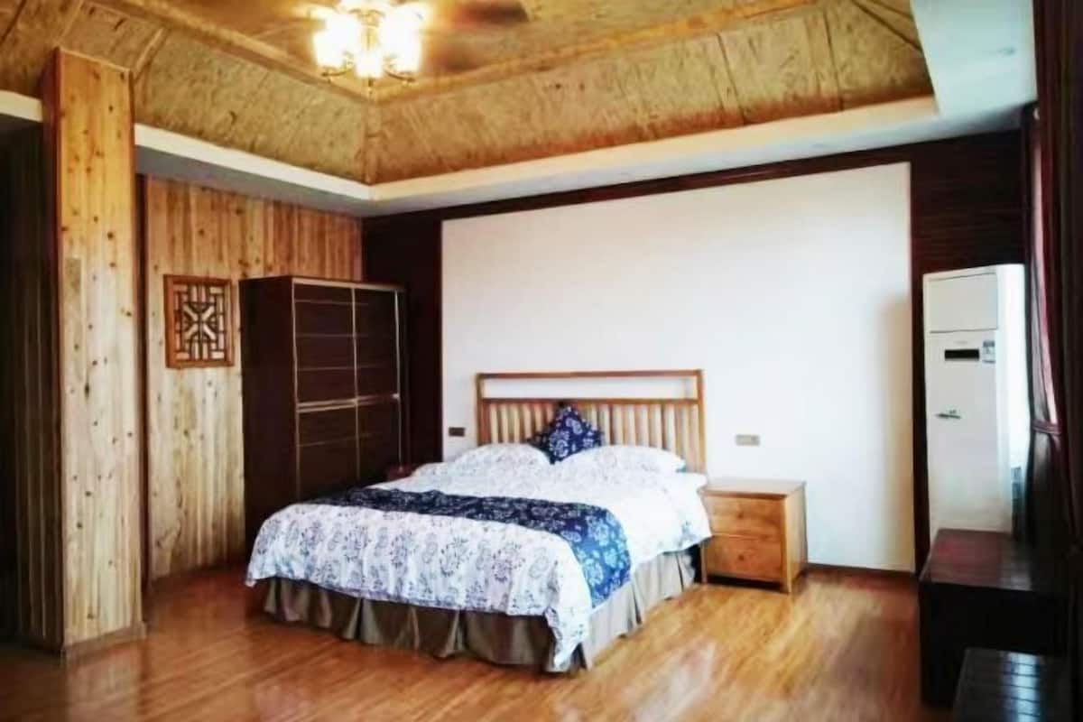A bedroom with a wooden ceiling, a bed with a patterned bedspread, a nightstand, and a wardrobe.