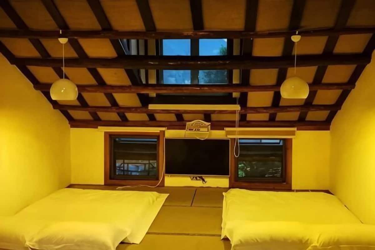A room with two beds, wooden beams on the ceiling, and windows.