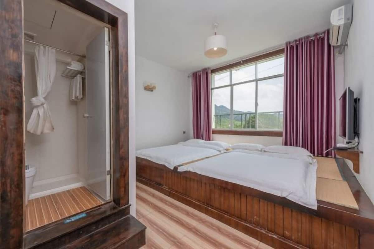 A room with a wooden bed, a window with curtains, a shower area, and a television.